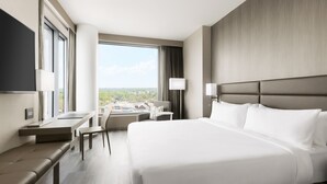 A modern hotel room with a large bed, a desk, and a chair. There is a window with a view of the city. - AC Hotel by Marriott Bethesda Downtown (Bethesda)