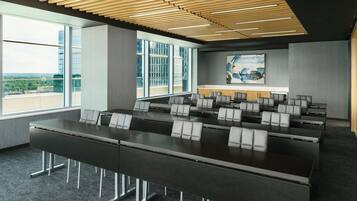 Un salón de conferencias con una larga mesa, numerosas sillas, ventanas amplias y un diseño moderno en el techo.