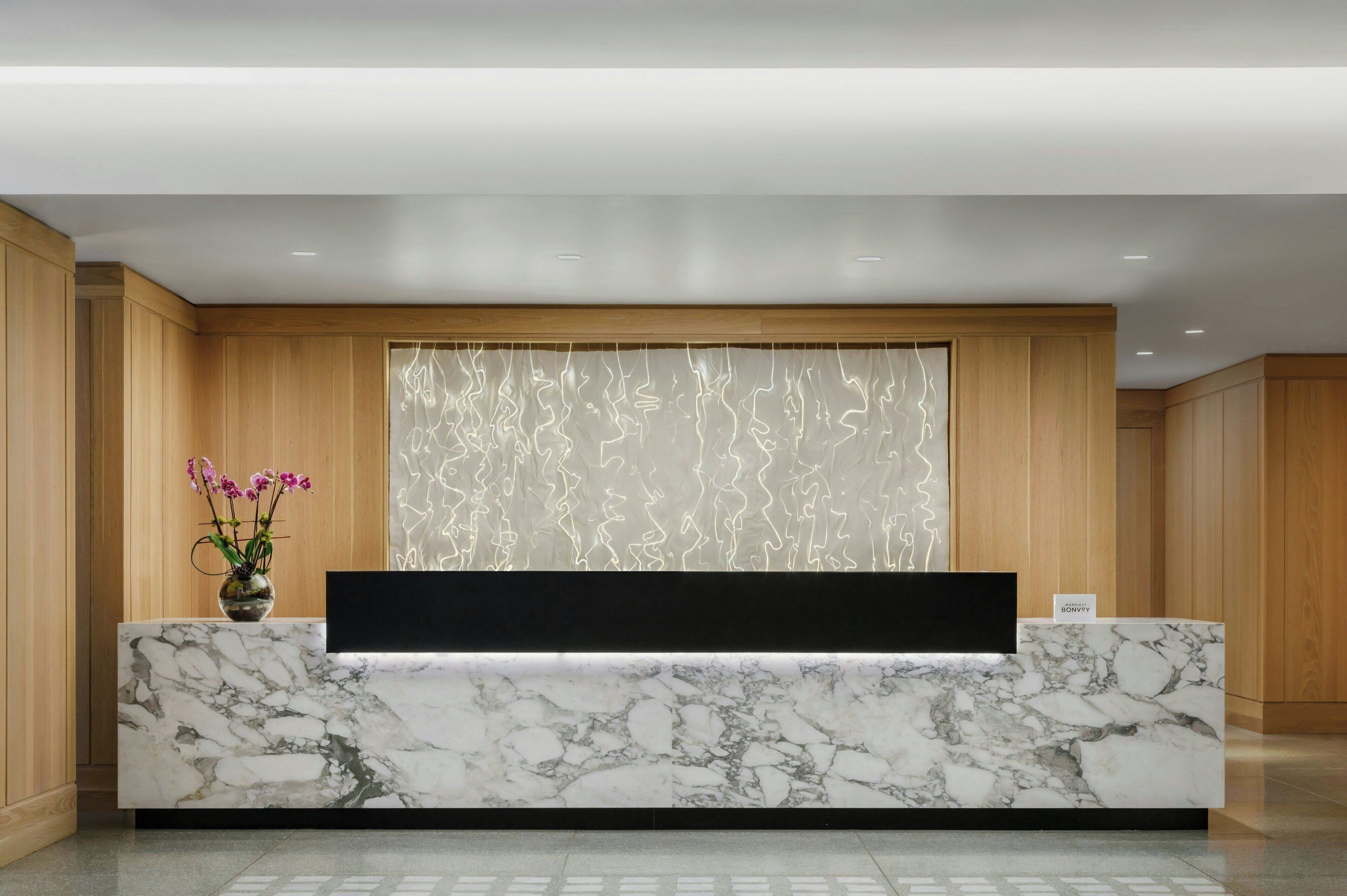 A reception desk with a marble top, a vase with flowers, and a wall with a light pattern.