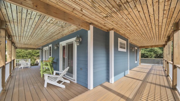 Una terraza de madera con techo, sillas blancas y una pequeña mesa.