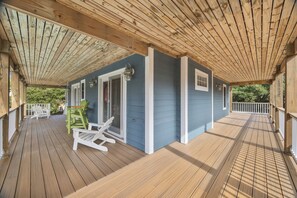 Una terraza de madera con techo, sillas blancas y una pequeña mesa.