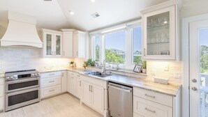 Una cucina moderna con mobili bianchi, elettrodomestici in acciaio inossidabile e ampie finestre che danno sulla campagna.