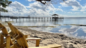Un pontile di legno con sedie rivolte verso un lago calmo, un molo che si estende nell'acqua e un gazebo in lontananza.