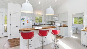 Une cuisine moderne avec des meubles blancs, un plan de travail en bois et des tabourets de bar rouges.