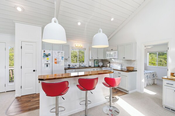 Una cocina moderna con armarios blancos, encimera de madera y taburetes rojos.