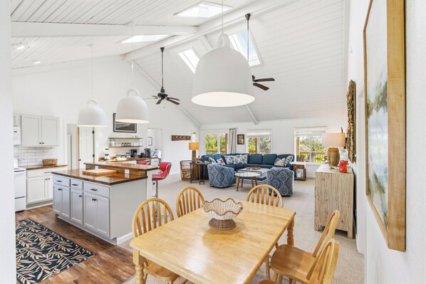 A spacious kitchen with a dining area, a living room with a sofa and a coffee table, and a large window providing natural light.