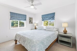 A bedroom with a bed, two bedside tables, a ceiling fan, and two windows with blue curtains.