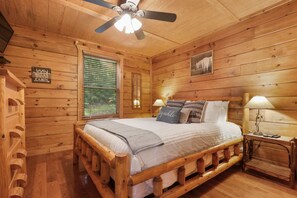 A wooden cabin bedroom with a bed, two bedside lamps, a ceiling fan, and a window with blinds. - Great Smokies Adventure Cabin w/Hot Tub and Deck! (Sevierville)