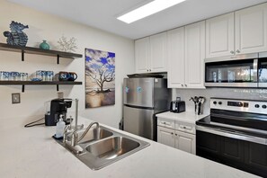 A modern kitchen with stainless steel appliances, white cabinetry, and a marble countertop.