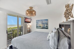 Un dormitorio con una cama grande, televisión, un cuadro y un balcón con vistas.