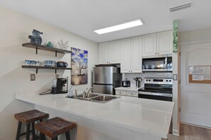 Une cuisine moderne avec des armoires blanches, un réfrigérateur en acier inoxydable, un four à micro-ondes et une cuisinière. On trouve deux tabourets en bois au comptoir.