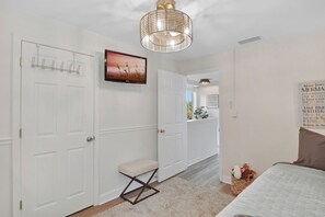 A bedroom with a bed, a bedside table, a chair, a television, and a door.