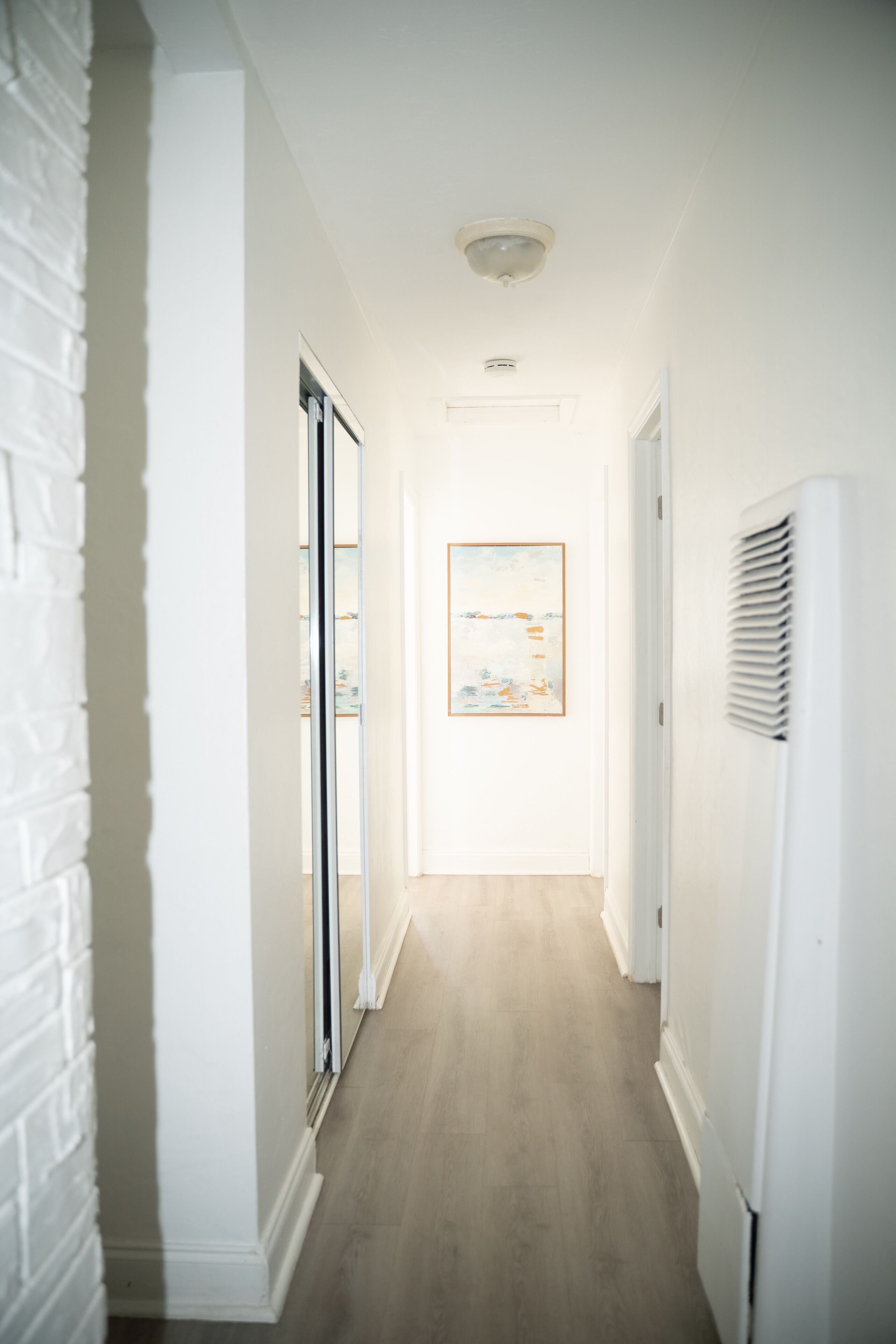A hallway with a white brick wall, a door with glass panels, and a framed picture on the wall.