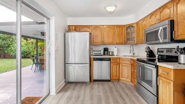 Une cuisine moderne avec des meubles en bois, des appareils électroménagers en acier inoxydable et une porte-fenêtre coulissante donnant sur un patio.