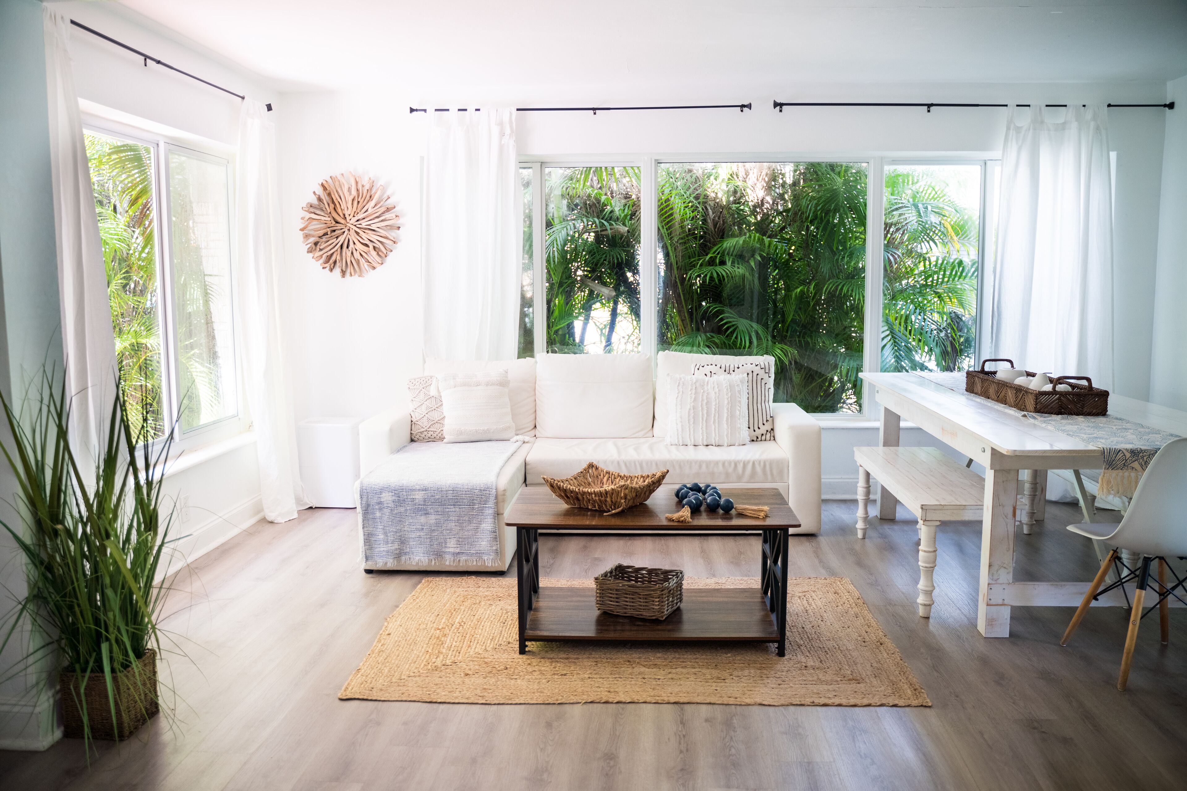 A bright living room with a white sofa, a wooden coffee table, and a view of lush greenery outside.
