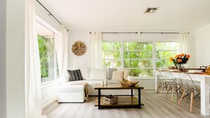 Un salon lumineux avec un canapé blanc, une table basse en bois et un coin repas comprenant une table et des chaises blanches.