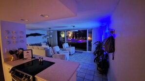 Ein modernes Wohnzimmer mit Küchenbereich, Blick auf den Pool und einem Balkon mit Poolblick.