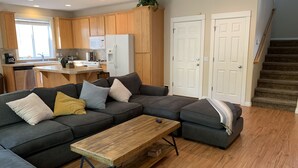 A modern living room with a sectional sofa, a wooden coffee table, and a kitchen area with wooden cabinets and a refrigerator. - Miller Hill Sanctuary near Intel w/ BBQ & Firepit (Aloha)