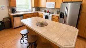 A modern kitchen with wooden cabinets, a stainless steel refrigerator, a microwave, a stove, and two bar stools. - Miller Hill Sanctuary near Intel w/ BBQ & Firepit (Aloha)