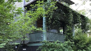 Una casa a due piani con un portico, immersa nel verde.