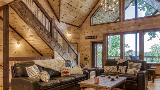 A spacious living room with a wooden staircase, leather sofas, and a large window offering a view of the outdoors.