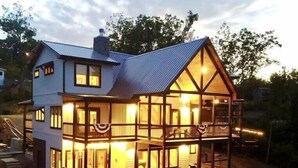 A two-story house with a balcony and a wrap-around porch, featuring multiple windows and a chimney.
