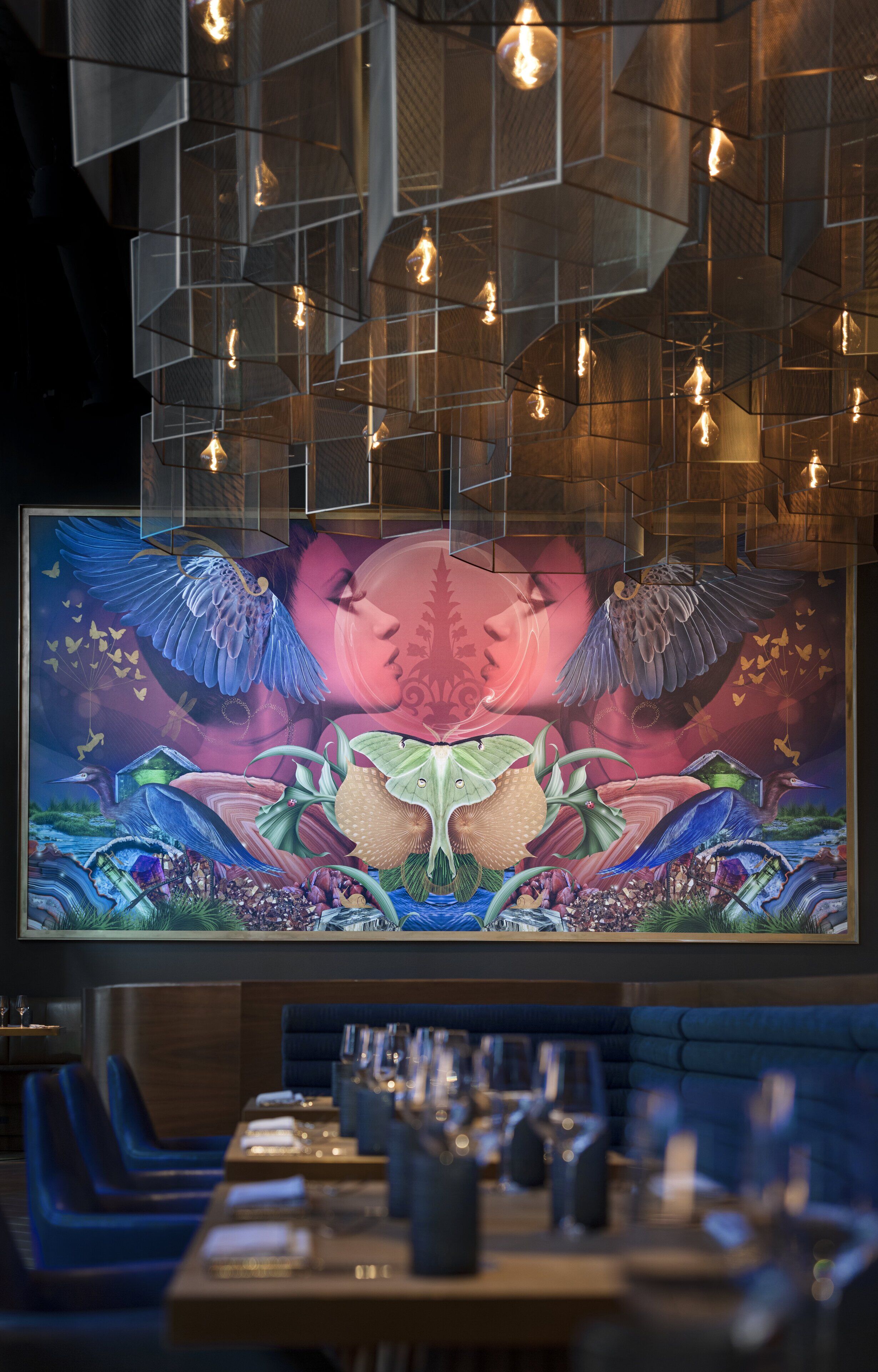 A restaurant with a large digital screen displaying a colorful mural, hanging pendant lights, and blue upholstered seating.