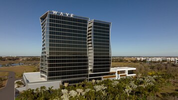 Un hôtel moderne, reconnaissable à son grand panneau « WAVE » placé en haut, avec une façade à motifs géométriques et un toit plat.