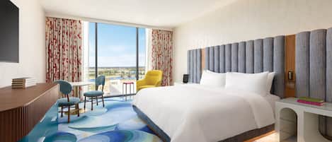 A modern hotel room with a large bed, a desk, and a view of the city.