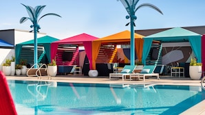 A pool area with multiple sun loungers and umbrellas, a clear pool, and potted plants.