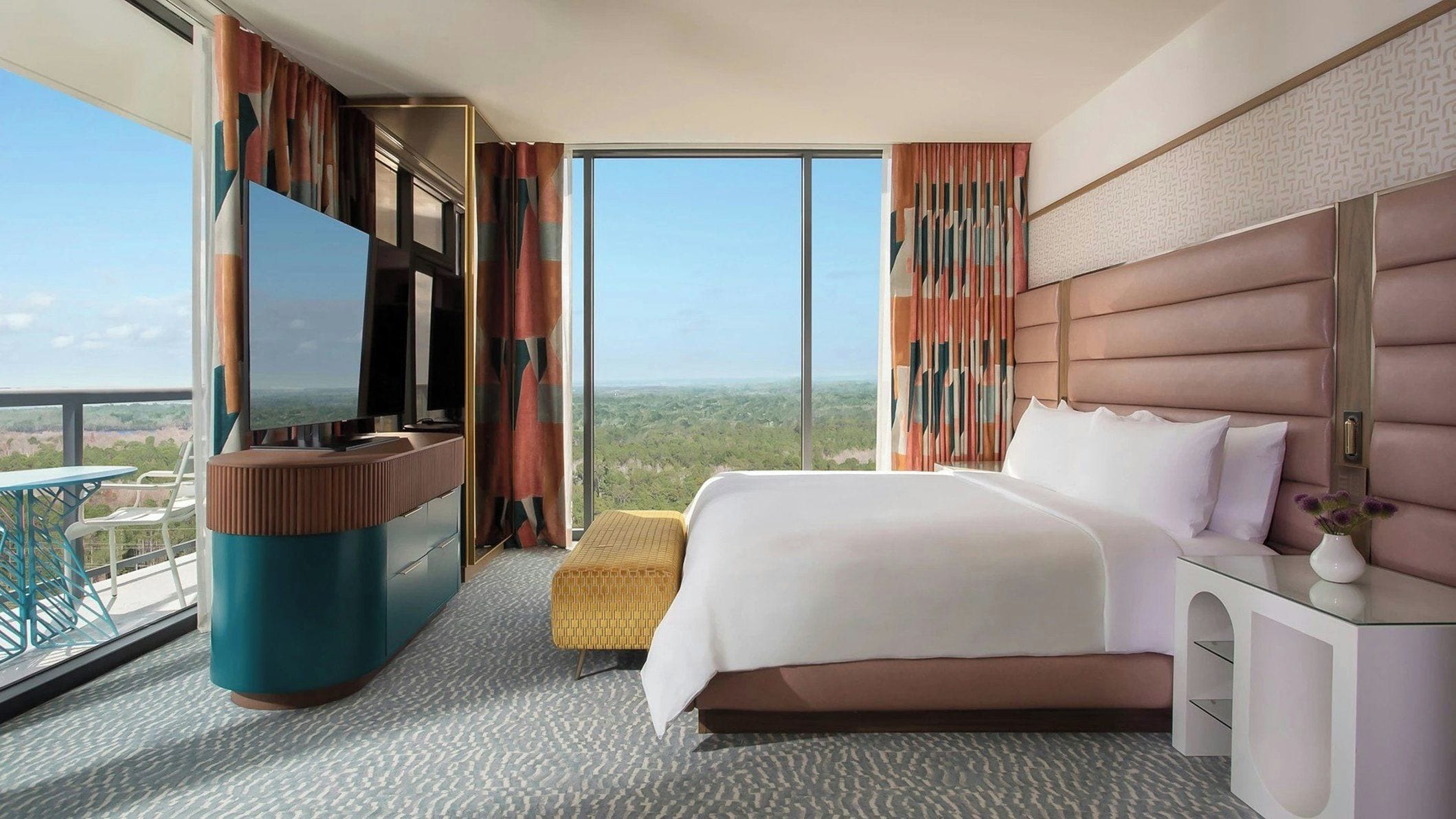 Ein Hotelzimmer mit einem großen Bett, einem Fernseher, einem Schreibtisch und einem Balkon mit Blick.