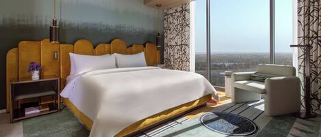 A modern hotel room with a large bed, a view of the landscape, a seating area, and a nightstand with books.