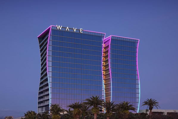 Un hotel moderno con un letrero 'WAVE', que presenta una fachada de vidrio y un diseño curvo.