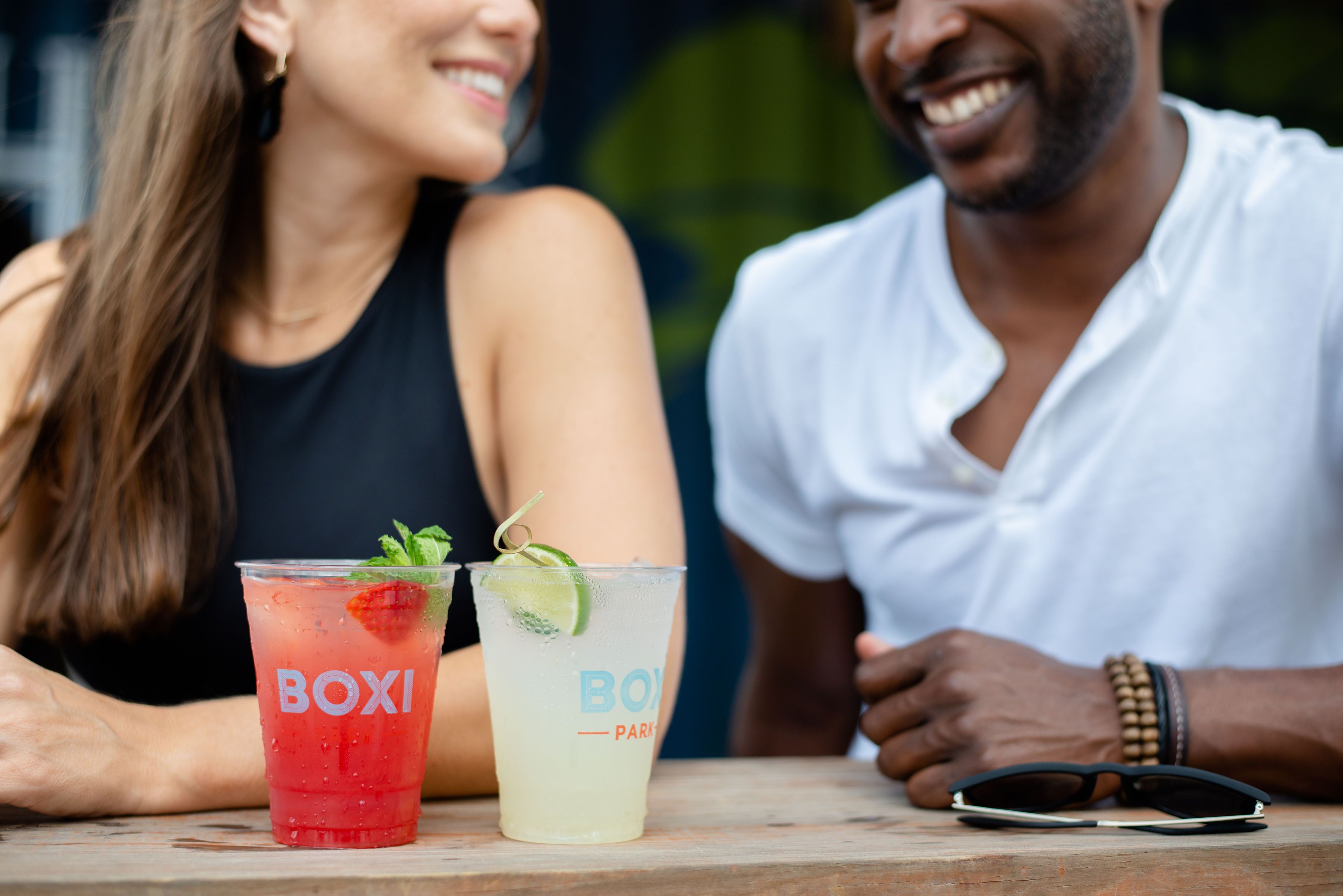 To personer sidder ved et bord med drikkevarer mærket 'BOXI' og 'BOY PARK'.