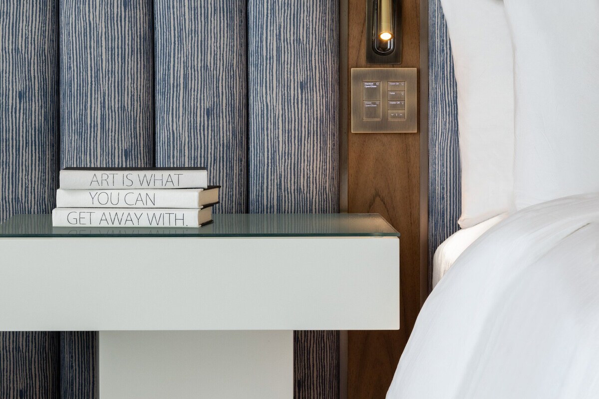 A neatly arranged bedside table with a stack of books and a wall-mounted light switch.