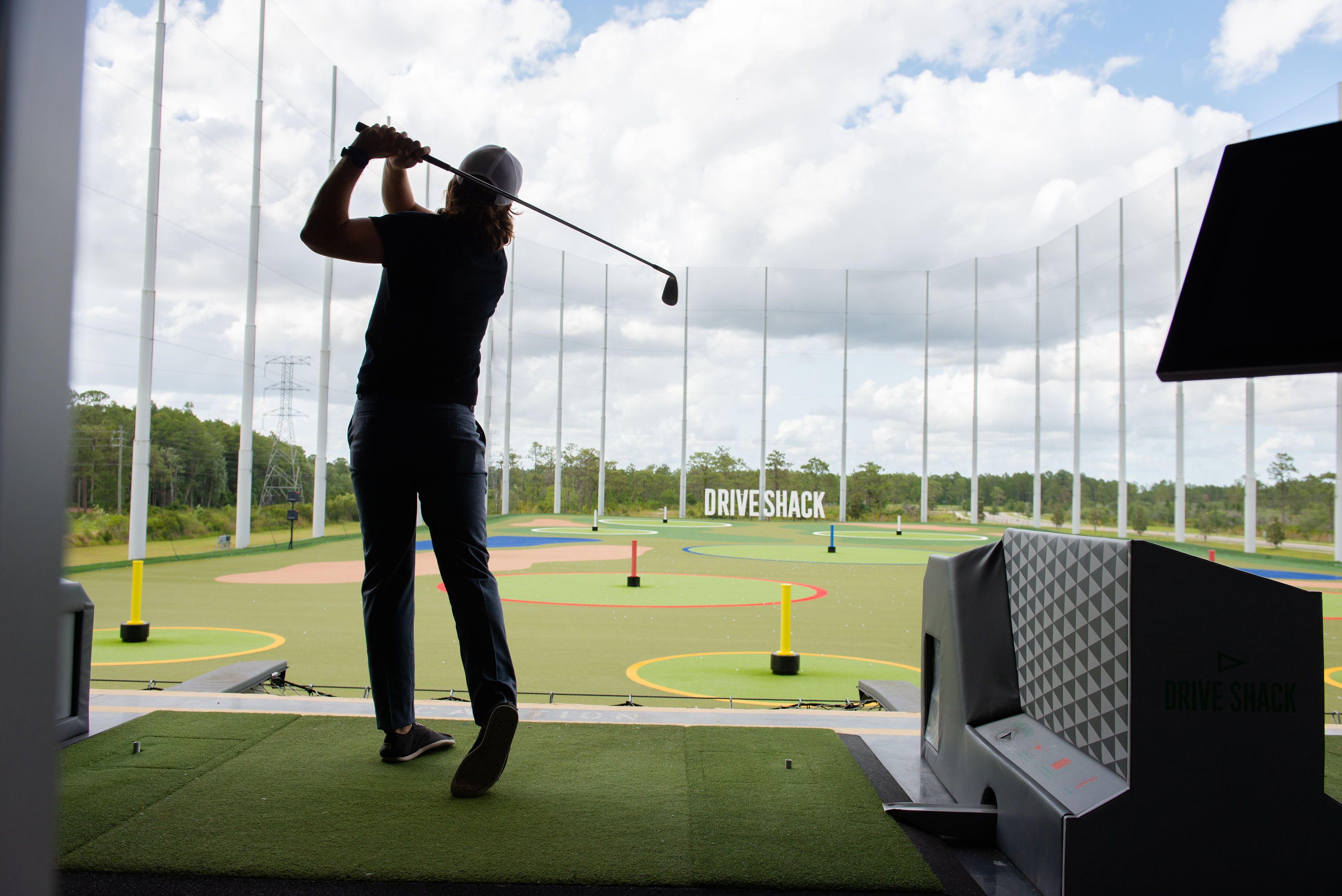 A golf driving range with a driving cage and a screen displaying "DRIVESHACK".