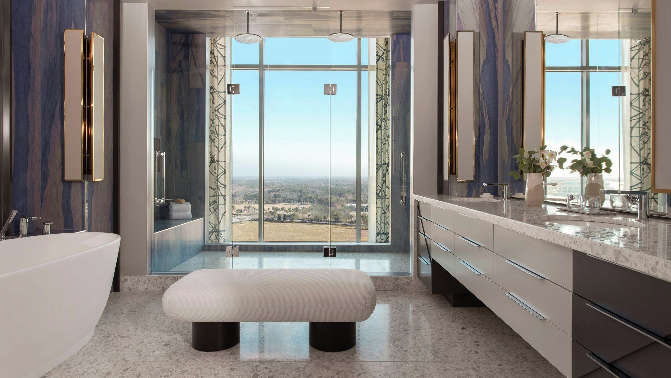 A modern bathroom with a large window, a bathtub, a vanity with a mirror, and a bench.
