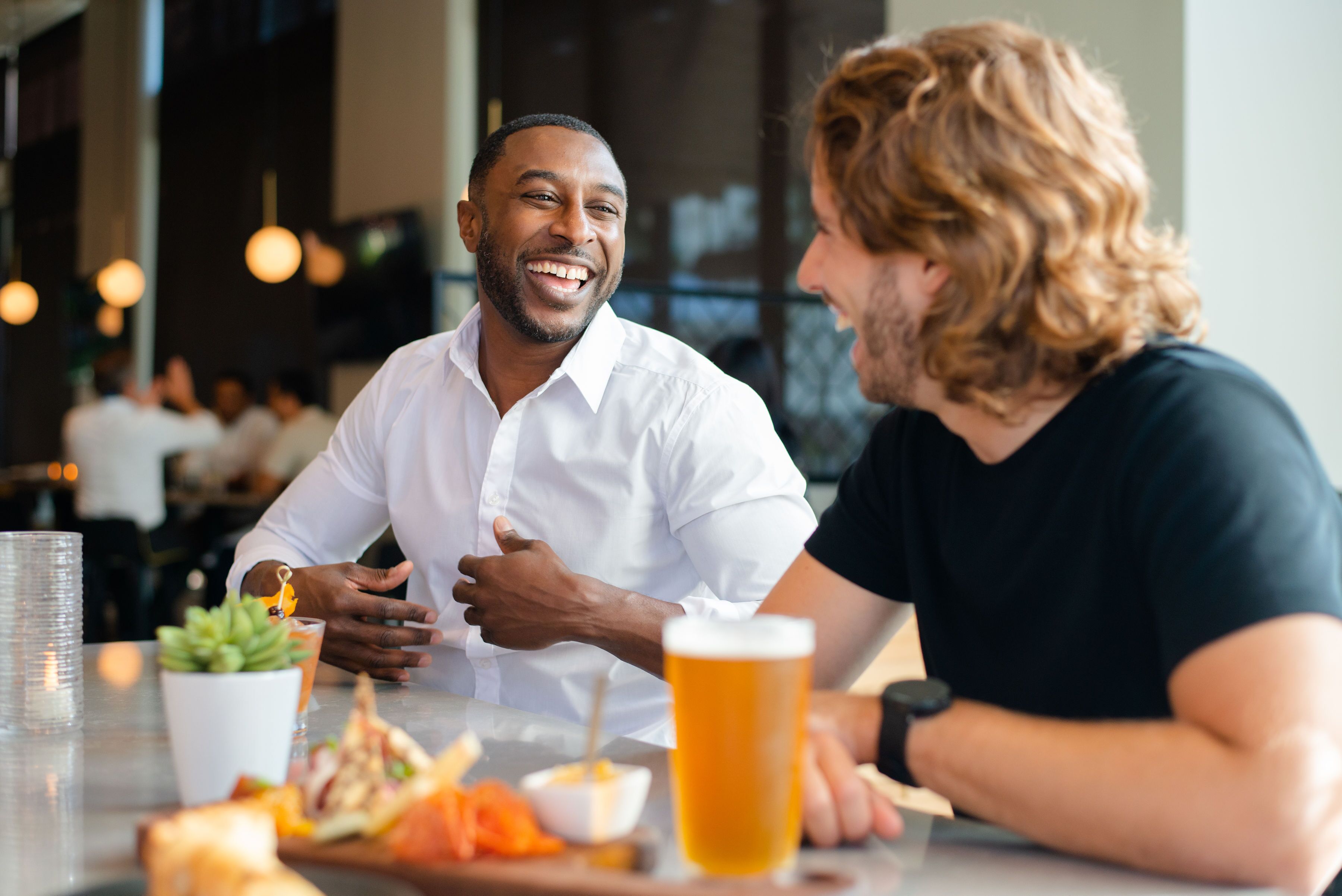Dos personas sentadas en una mesa con una jarra de cerveza, un cuenco pequeño y una planta.