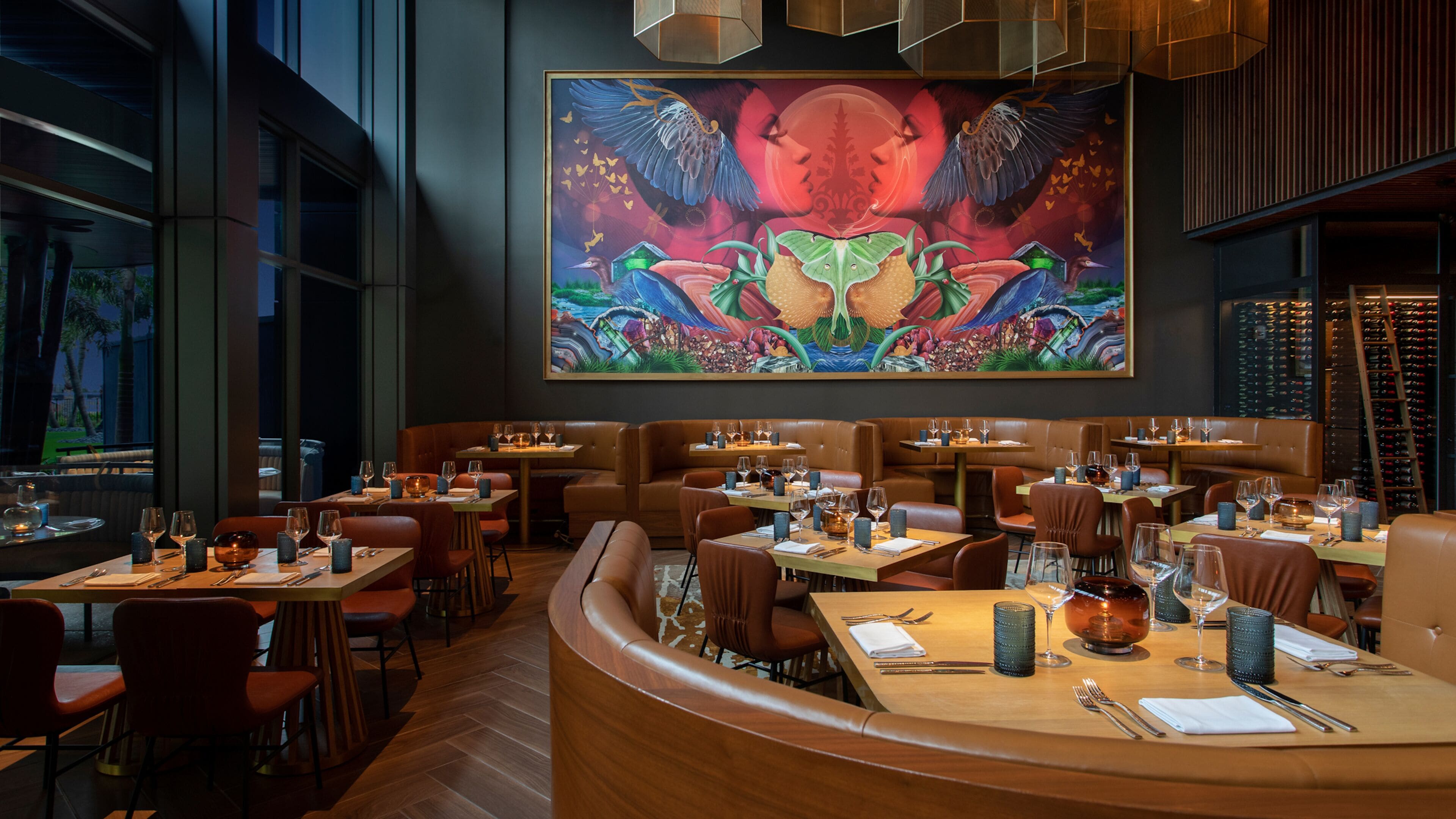 A restaurant with multiple seating areas, including booths and tables, and a large mural on the wall.