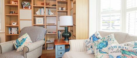 A cozy living room with a sofa, armchair, and a wooden bookshelf filled with books and decorative items.