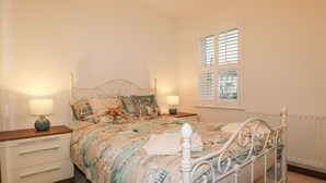Une chambre à coucher avec un lit, deux tables de chevet, une fenêtre avec des volets et un radiateur.