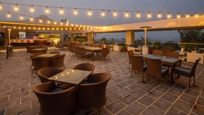 Un patio al aire libre con mesas y sillas, luces colgantes y vistas al paisaje.