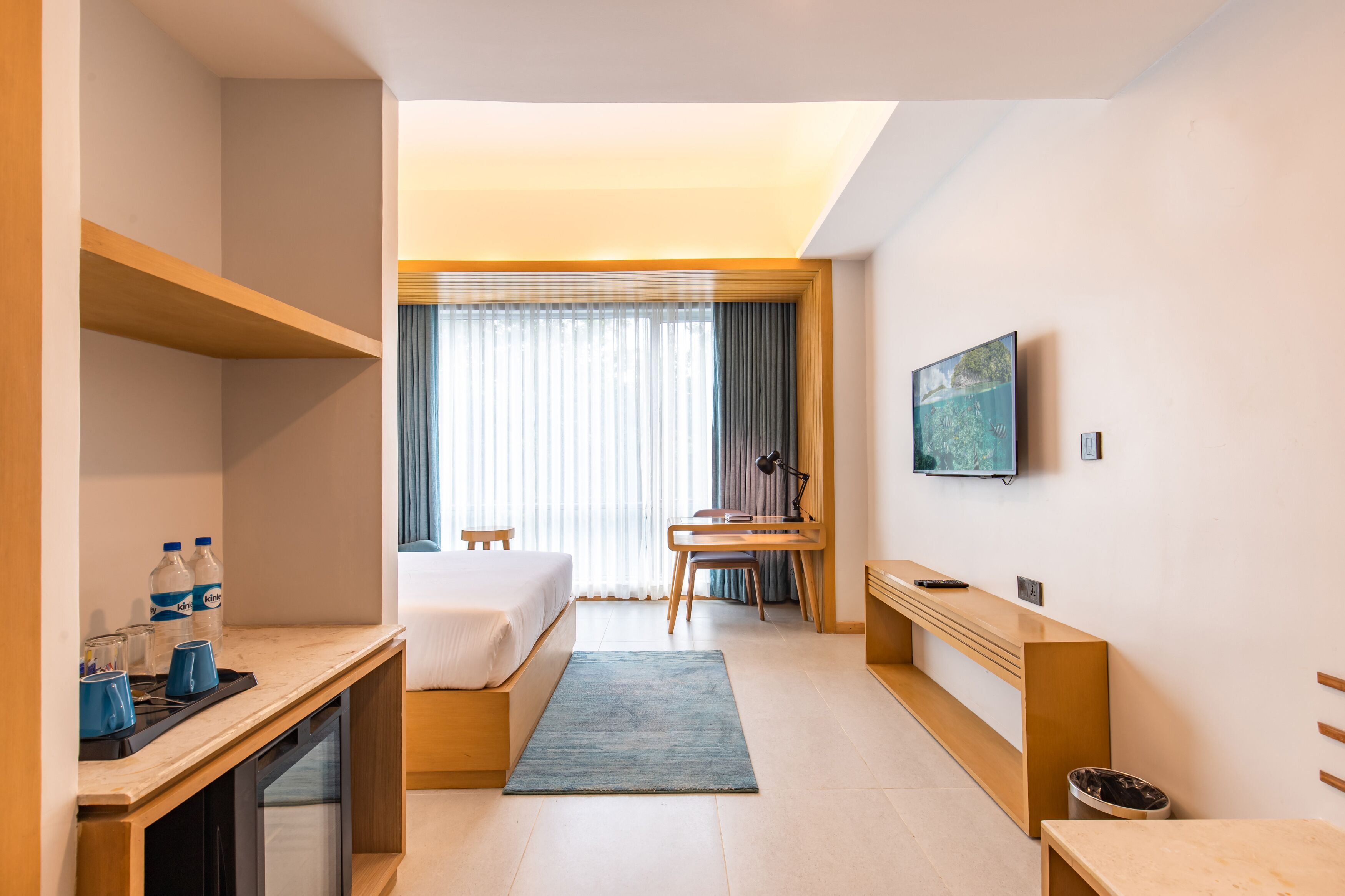 A hotel room with a bed, desk, and chair, a television, and a window with curtains.