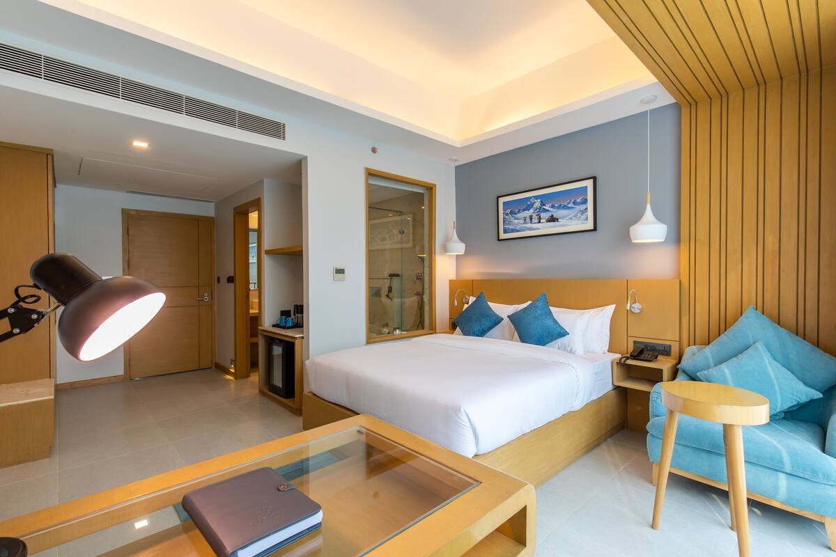A modern hotel room with a large bed, a glass coffee table, a sofa, and a desk with a lamp.