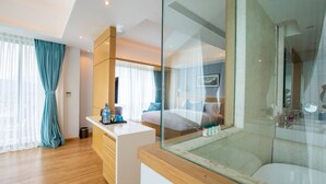 Una habitación de hotel moderna con una cama grande, cabina de ducha con paredes de vidrio, un escritorio de madera y vistas a la ciudad.