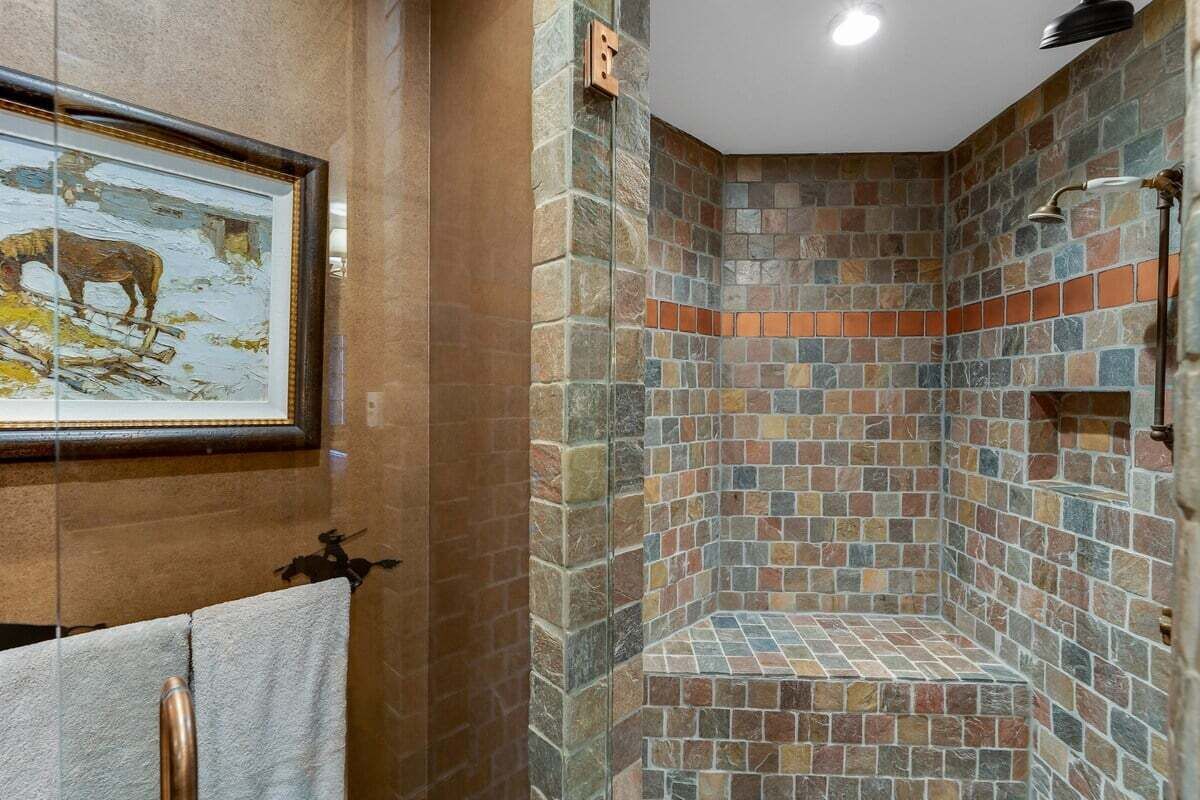 A bathroom with a stone mosaic shower, a framed painting on the wall, and a towel rack.