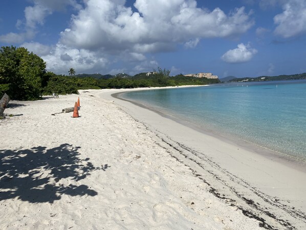 Uma praia com águas turquesa cristalinas, areal arenoso e algumas árvores.