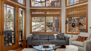 A spacious living room with a large window, a glass coffee table, a gray sofa, and a beige armchair.