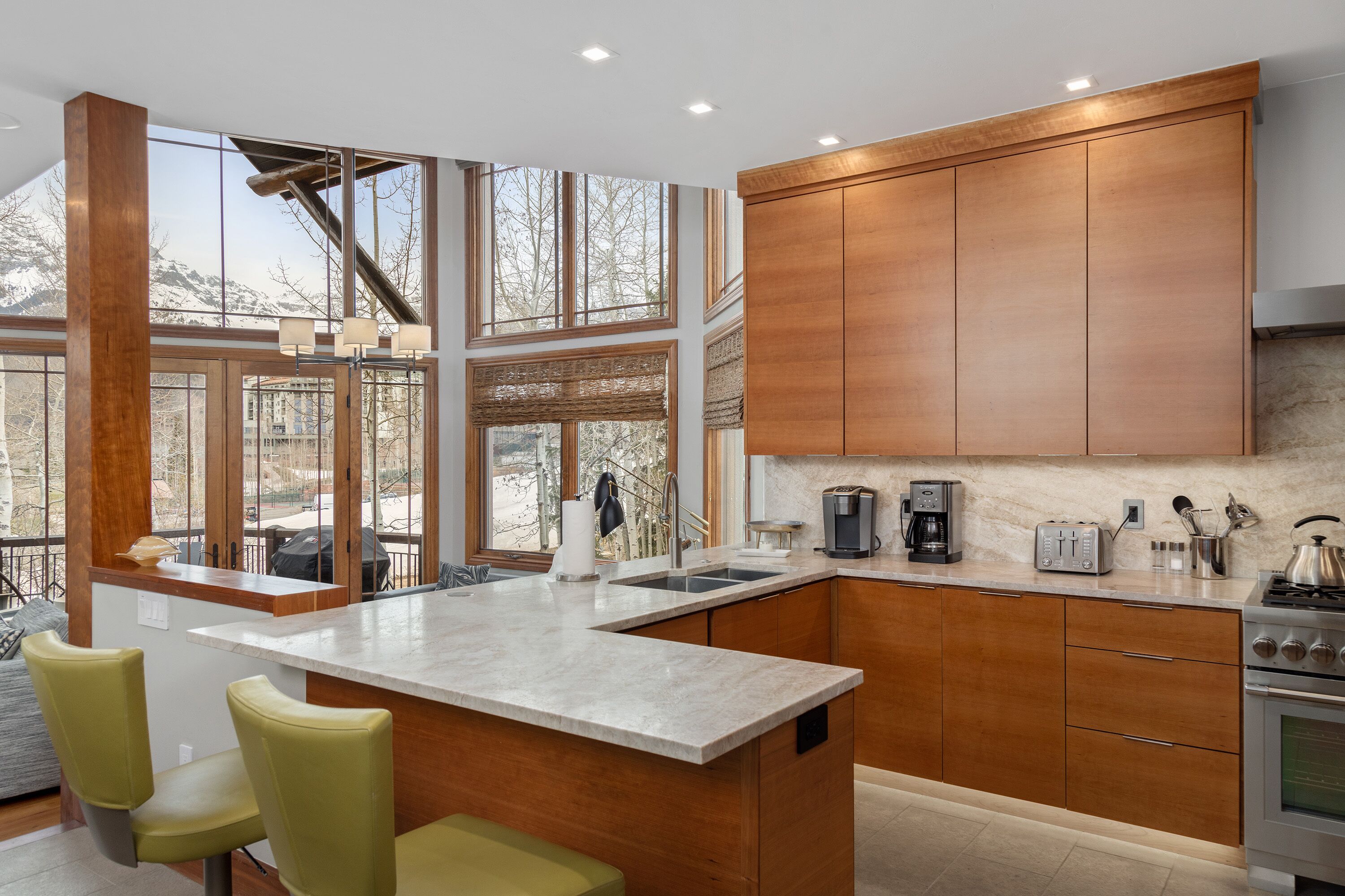 A modern kitchen with a large island, wooden cabinets, and a view of mountains.