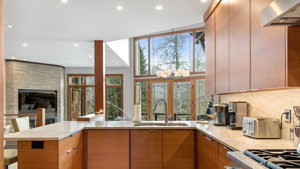 A modern kitchen with a large island, built-in appliances, and large windows offering views of the outdoors.